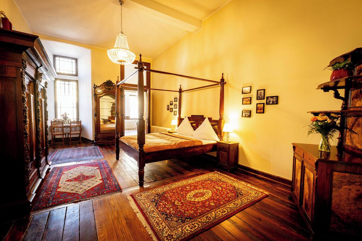 Un dormitorio tradicional con cama con dosel, pisos de madera y un candelabro.