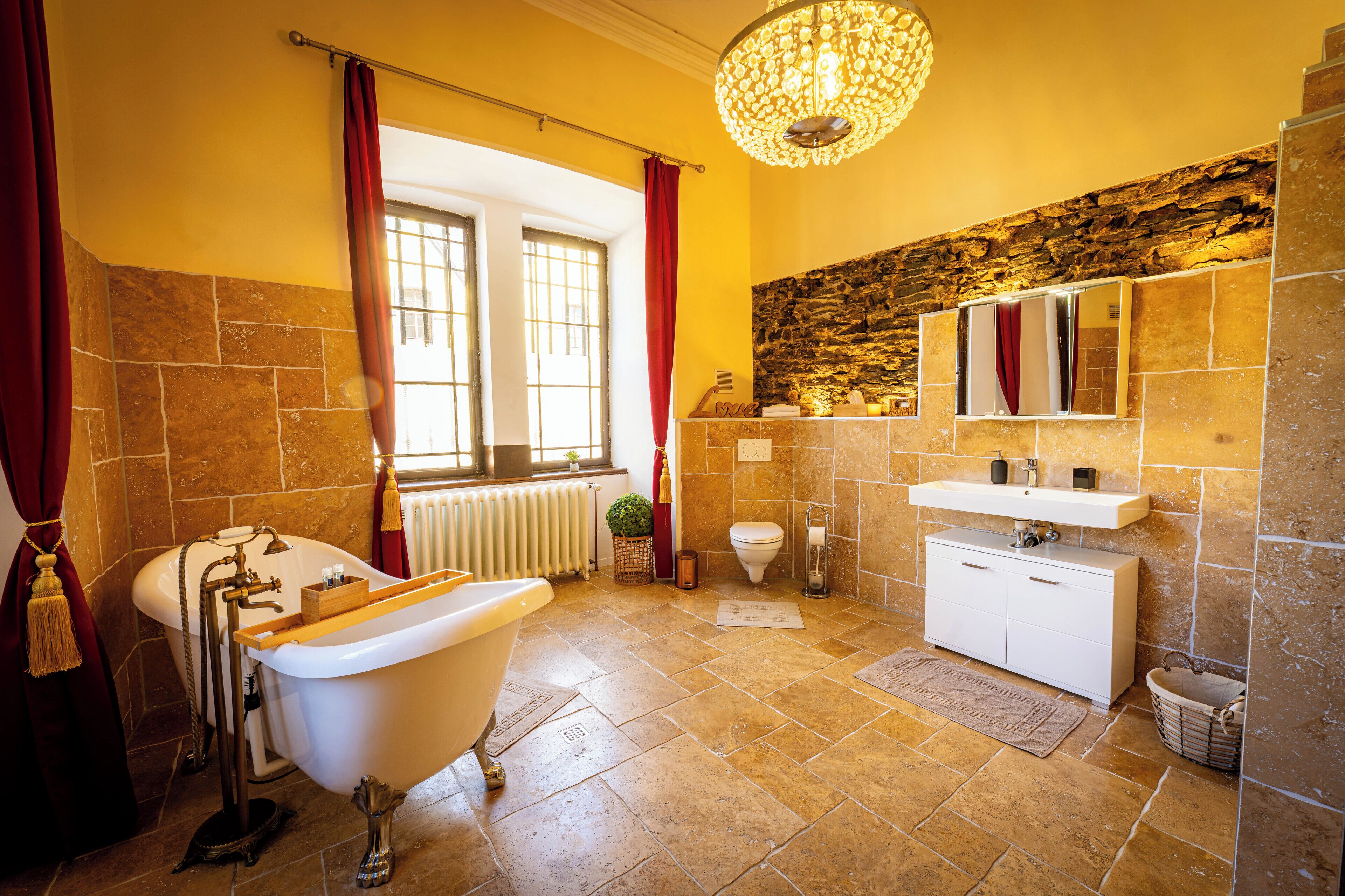 Een badkamer met een ligbad op pootjes, een witte wastafel, een spiegel boven de wastafel en een stenen muur.
