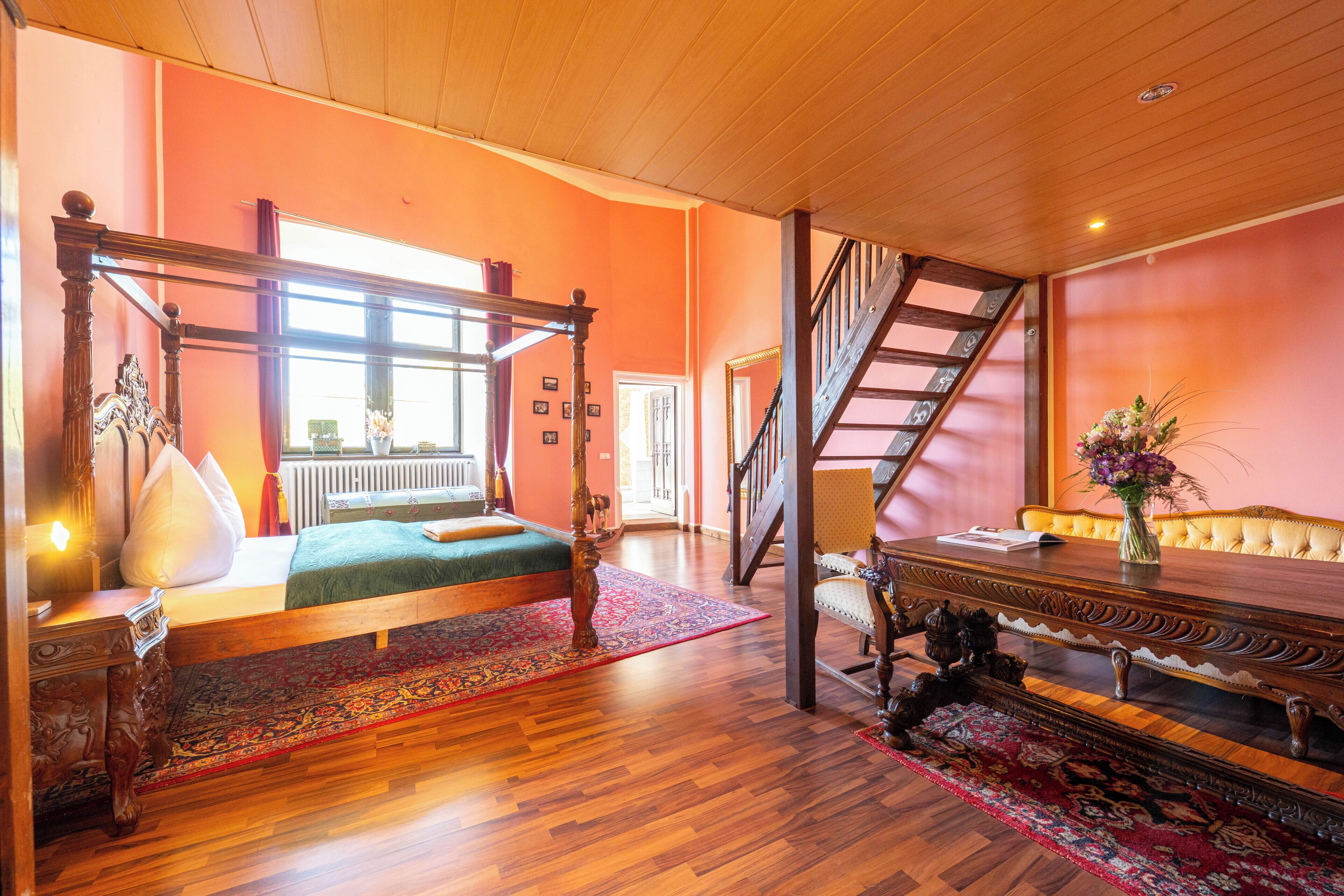 A room with a four-poster bed, a wooden staircase, and a dining table with a vase of flowers.