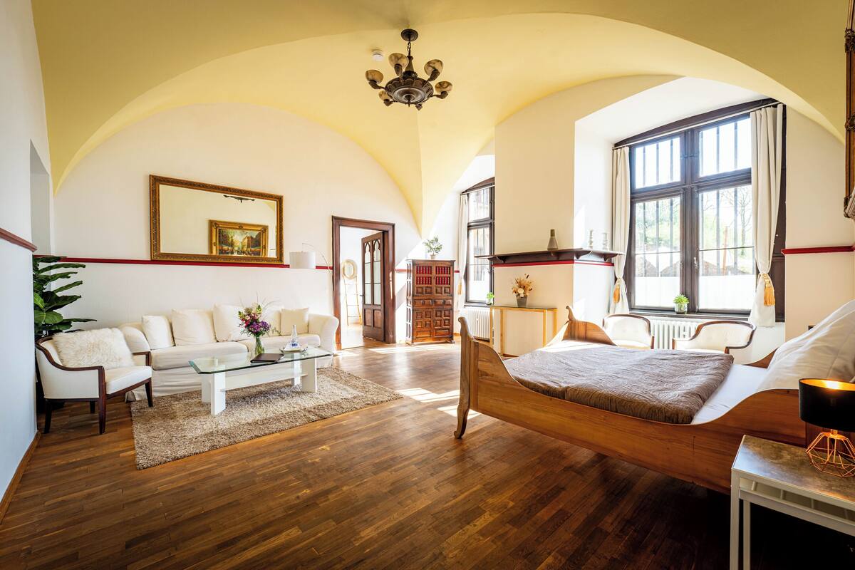 Una habitación amplia con una cama grande, un sofá, una mesa de centro y una araña.