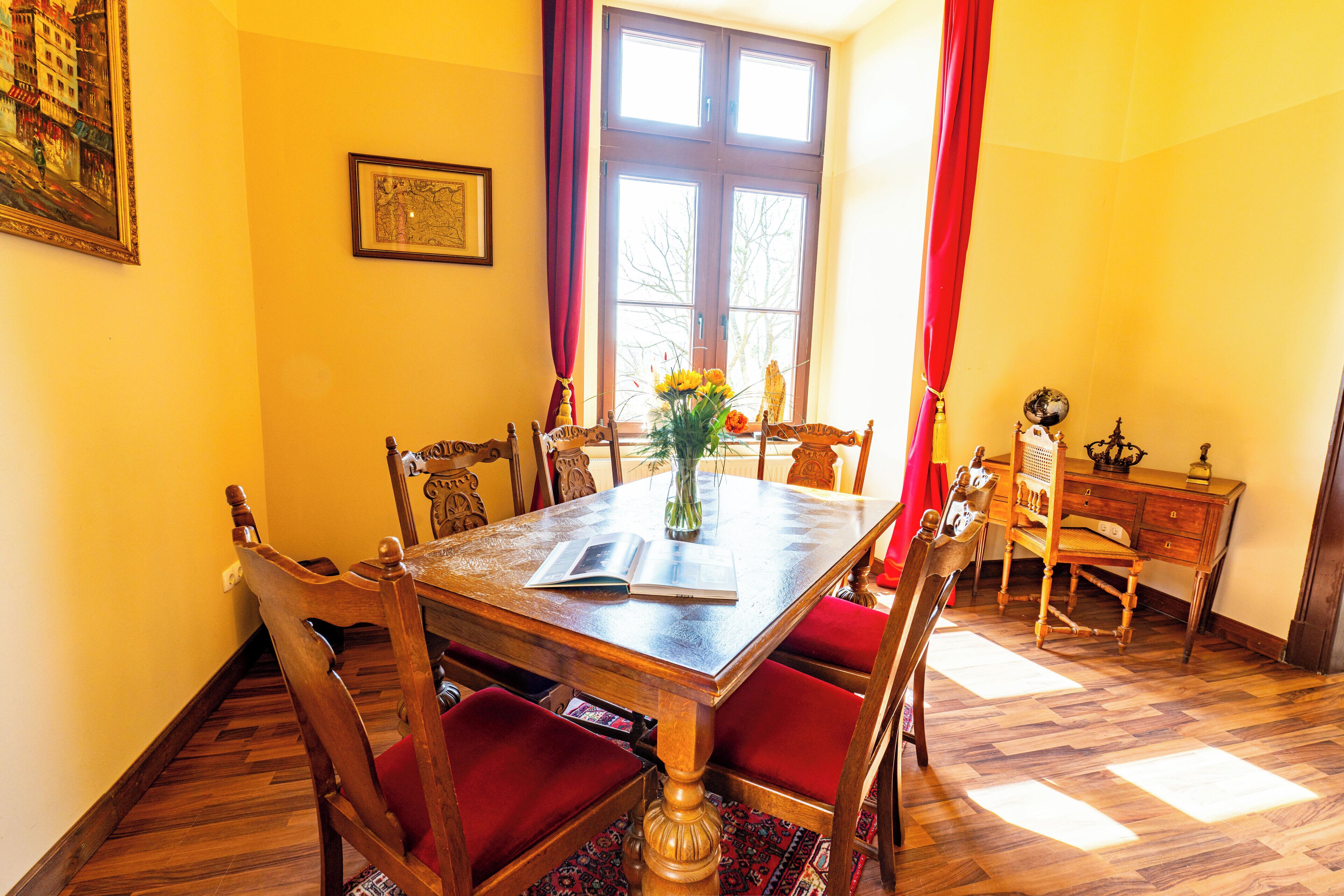 A dining area with a wooden table, red upholstered chairs, a vase with flowers, and a globe on a wooden side table.