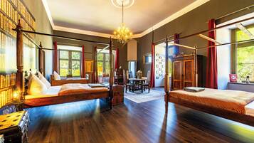 A room with two beds, a chandelier, wooden floors, and a bookshelf.