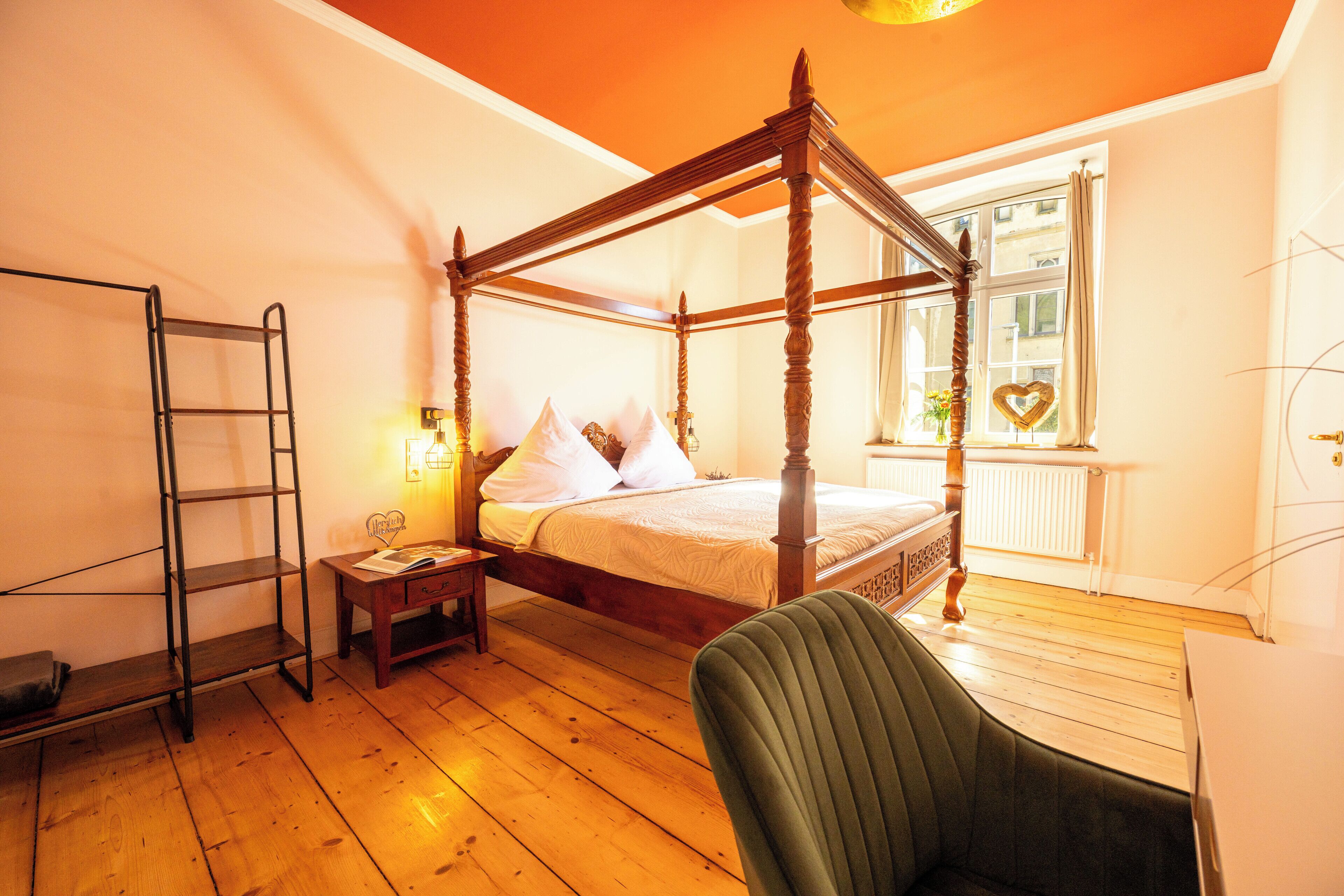 A four-poster bed in a room with wooden flooring, a ladder, a bedside table, and a chair.