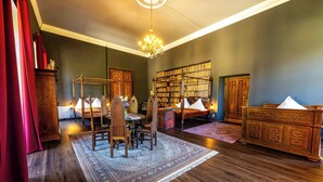 Une pièce avec un plancher en bois, un lustre, une bibliothèque et un rideau rouge.