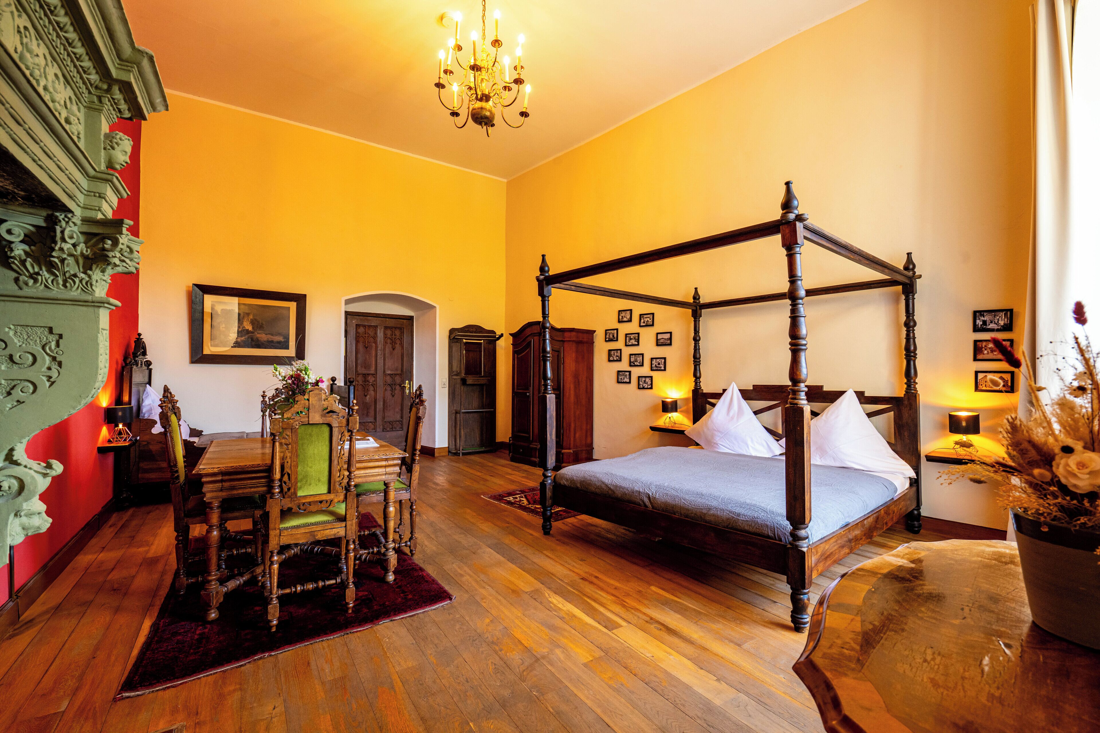A four-poster bed with white linens, a wooden table with chairs, and a chandelier.