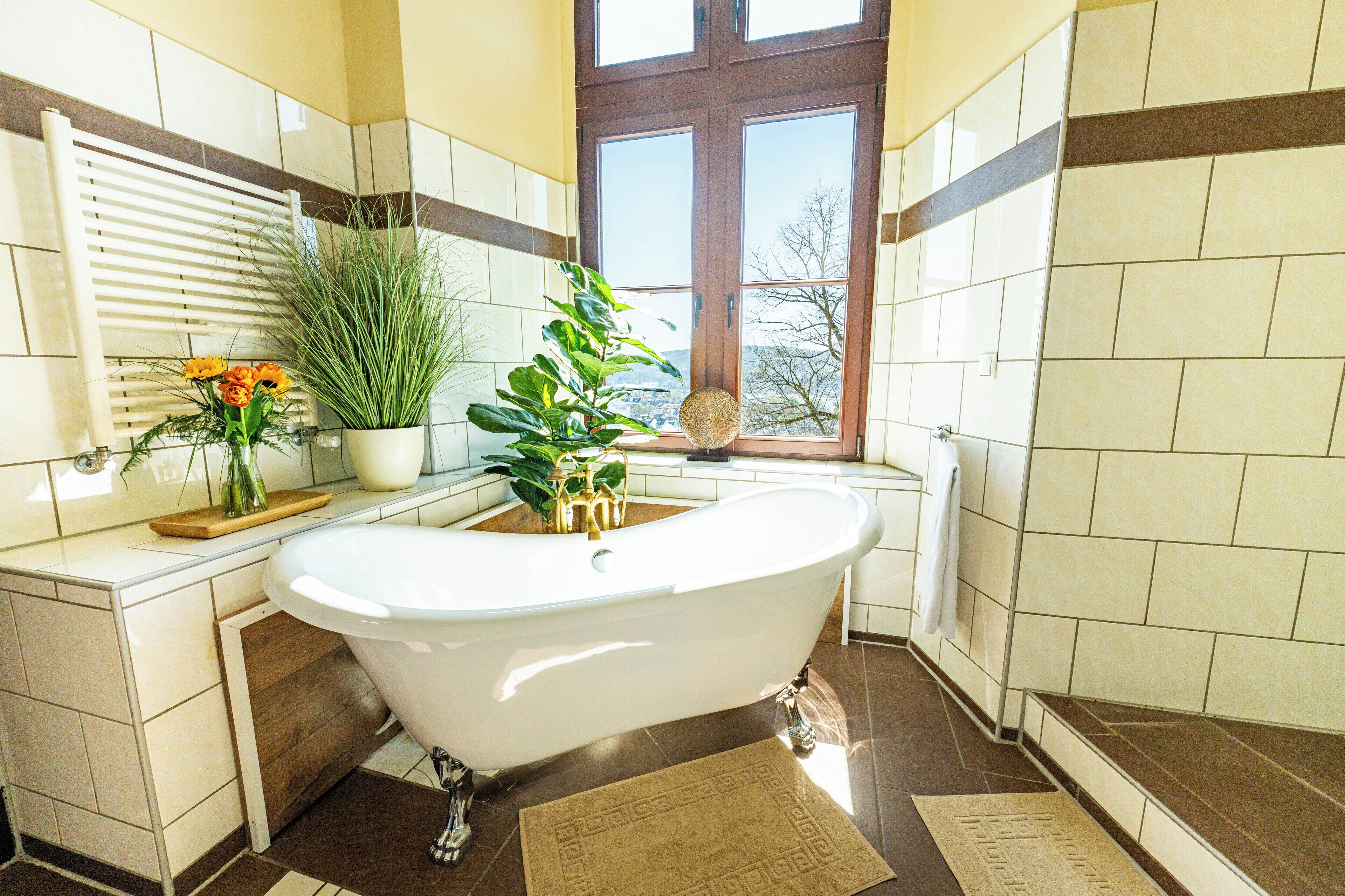 Een badkamer met een vrijstaand bad, een raam met uitzicht en een plant in een pot op het aanrecht.