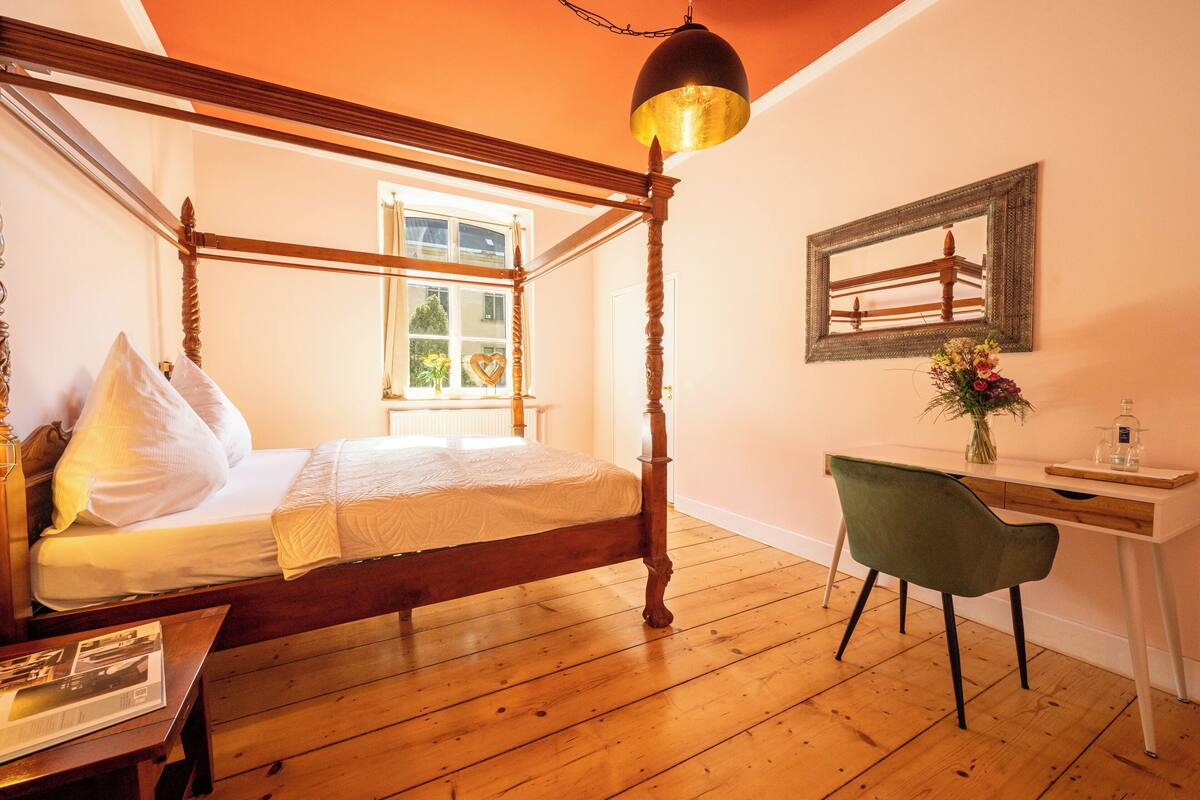 Una cama con dosel de madera, un escritorio con una silla y un espejo en la pared.