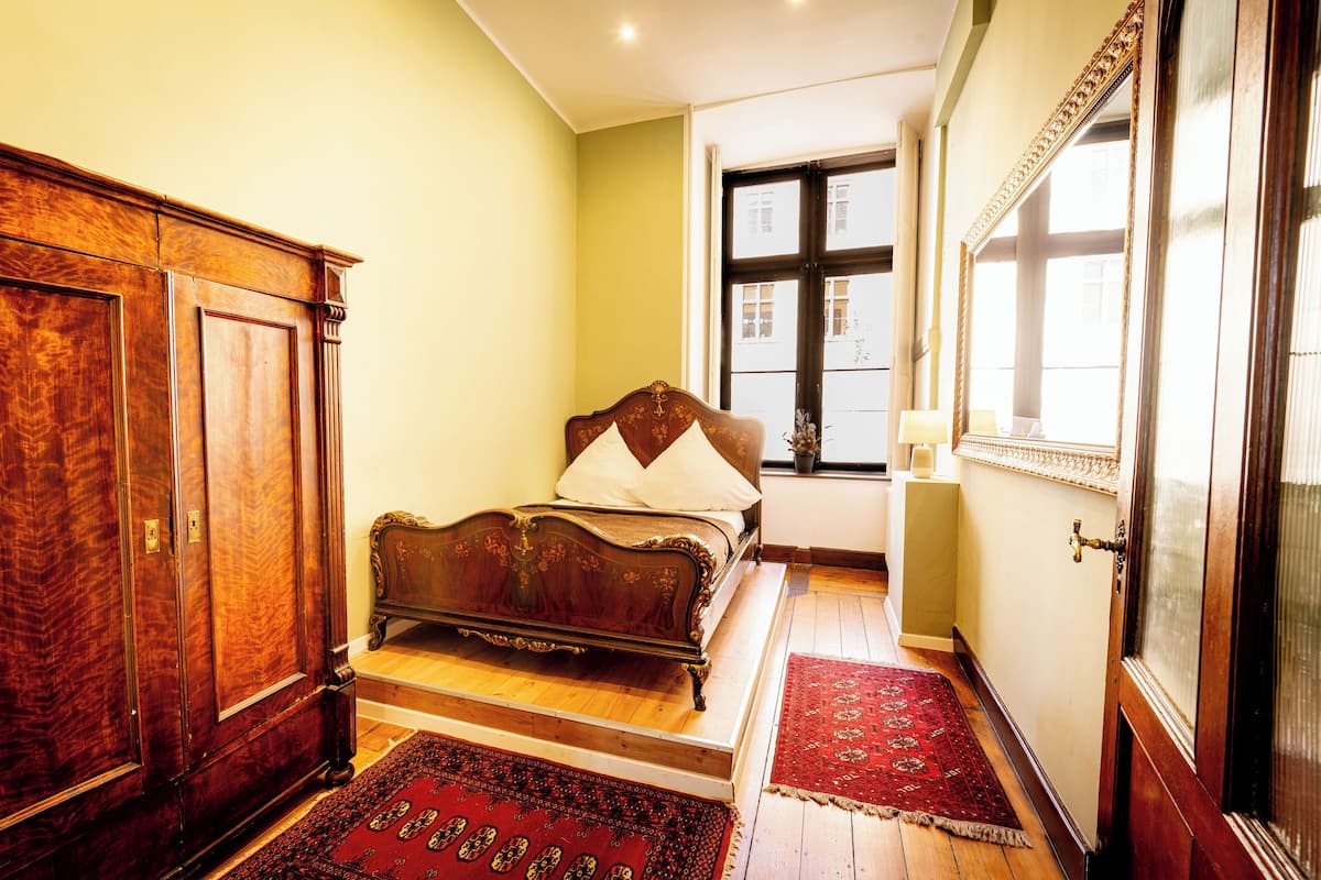 Un dormitorio con cama de madera, un armario, una ventana con vistas y un tapete rojo estampado.