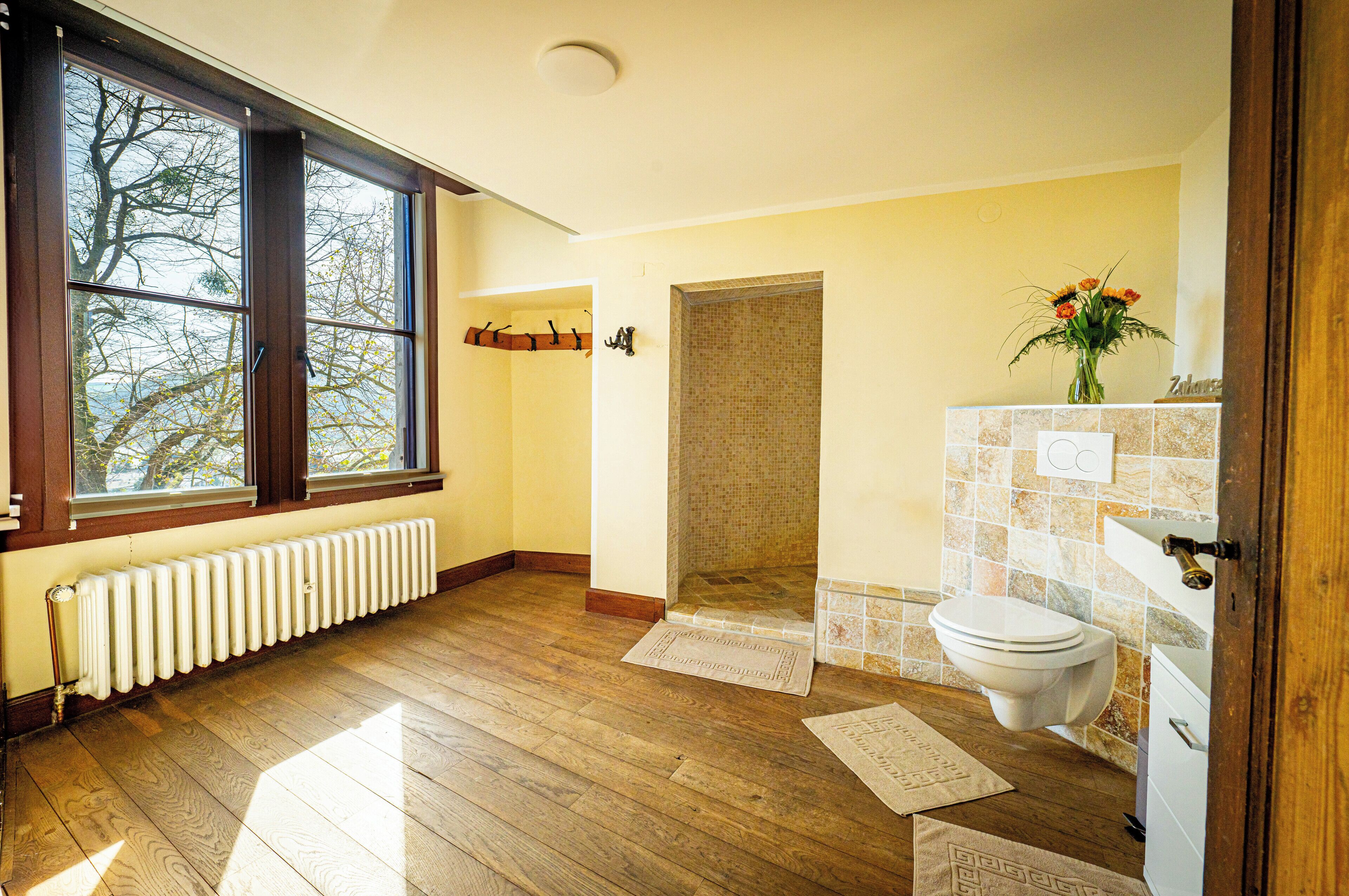 A bathroom with a wooden floor, a white radiator, a toilet, and a shower area.
