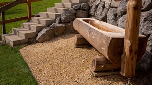 A wooden log chute leading to a stone basin, surrounded by a wooden fence and steps. - Chalet Annabelle (Sankt Stephan)