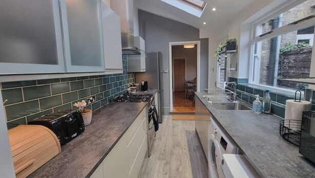 A modern kitchen with a central island, a built-in oven, and a window overlooking a garden. - Pet friendly comfortable Victorian terraced home (Cambridge)