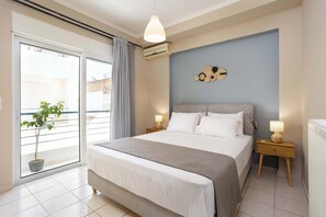 A bedroom with a bed, bedside tables, a wall-mounted air conditioner, a potted plant, and a view through a sliding door. - Kalamata City Nest, Ypapanti Cozy & Bright Getaway (Kalamata)