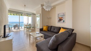 A living room with a grey sofa, a white coffee table, and a TV on a cabinet. There is a balcony with a view of the sea. - Beachfront House in Las Palmas With Sea Views (Las Palmas de Gran Canaria)