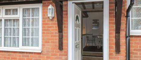 A brick cottage with a white door and windows, a sign reading "Claire Cottage," and a small table with chairs inside.