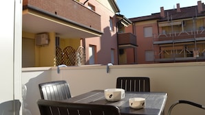 Un balcón con mesa y sillas, con vista a una zona residencial de edificios de ladrillo y cielo despejado.