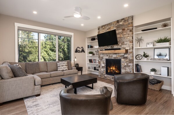 A modern living room with a stone fireplace, a large window, and a flat-screen TV.