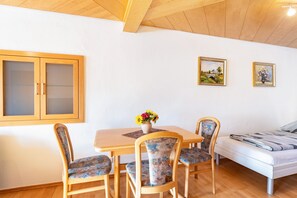A room with a wooden ceiling, a dining table with chairs, a bed, and two framed pictures on the wall.