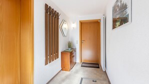 Un corridoio con una porta in legno, un termosifone, un piccolo mobile in legno con una pianta e uno specchio fissato al muro.