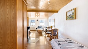 Una stanza con pavimento in legno, un letto, un tavolo da pranzo con sedie, un divano e un angolo cottura con fornello e frigorifero.