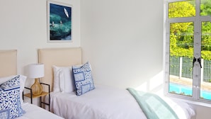 A hotel room with two beds, a window with a view of a swimming pool, and a framed picture on the wall. - Tranquil 2BR w/ Balcony, Pool, Walk to Beach (Cape Town)