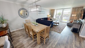 A spacious living area with a dining table, wooden chairs, a dark blue sofa, and a coffee table. - Beautiful ST 3025 New Rental! (Destin)