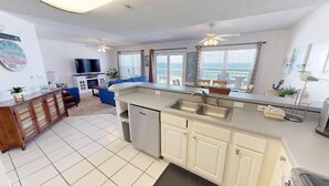 A modern kitchen with a dishwasher, double sink, and a dining area with a view of the ocean.