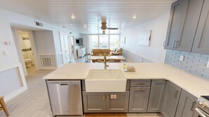 A modern kitchen with a dishwasher, sink, and a built-in oven. There is a dining area with a table and chairs, and a ceiling fan. - Gorgeous Dolphin Point 604C (Destin)