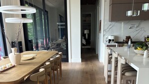 A modern kitchen with wooden flooring, a dining area with a large table and chairs, and a view into the dining room. - Luxury cottage (Port Carling)
