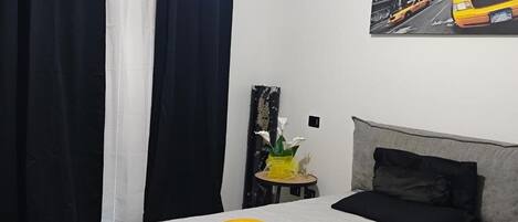 A hotel room with a bed, a small table with a vase of flowers, and a painting of a yellow taxi on the wall.