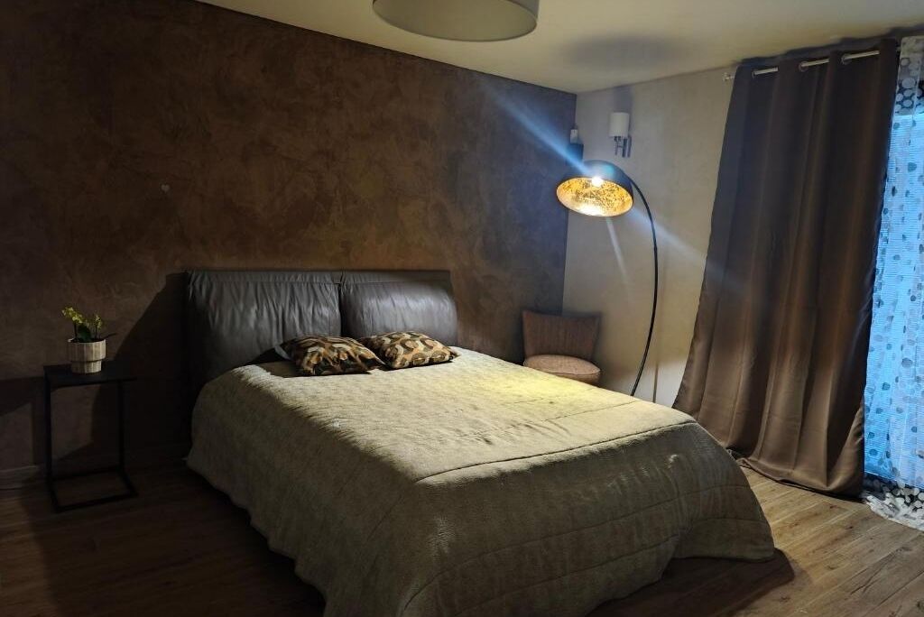 Ein Schlafzimmer mit einem großen Bett, einem Nachttisch mit Lampe und einem Fenster mit Vorhängen.