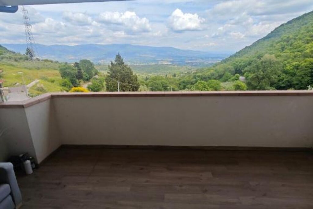 En balkon med udsigt over en grøn dal og bjerge.