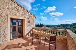 A stone building with a balcony, two wooden chairs, and a view of the countryside. - Country House 'Tolo' with Sea View, Private Pool and Wi-Fi (Son Servera)