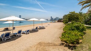 A beach with sun loungers and umbrellas, a clear sky, and a city skyline in the background. - Vogue | Palm Jumeirah with Access to Private Beach (Dubai)