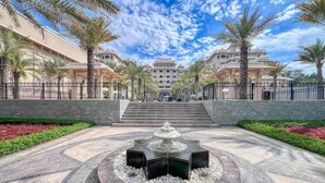 A grand hotel entrance with a central fountain, palm trees, and a clear sky. - Vogue | Palm Jumeirah with Access to Private Beach (Dubai)
