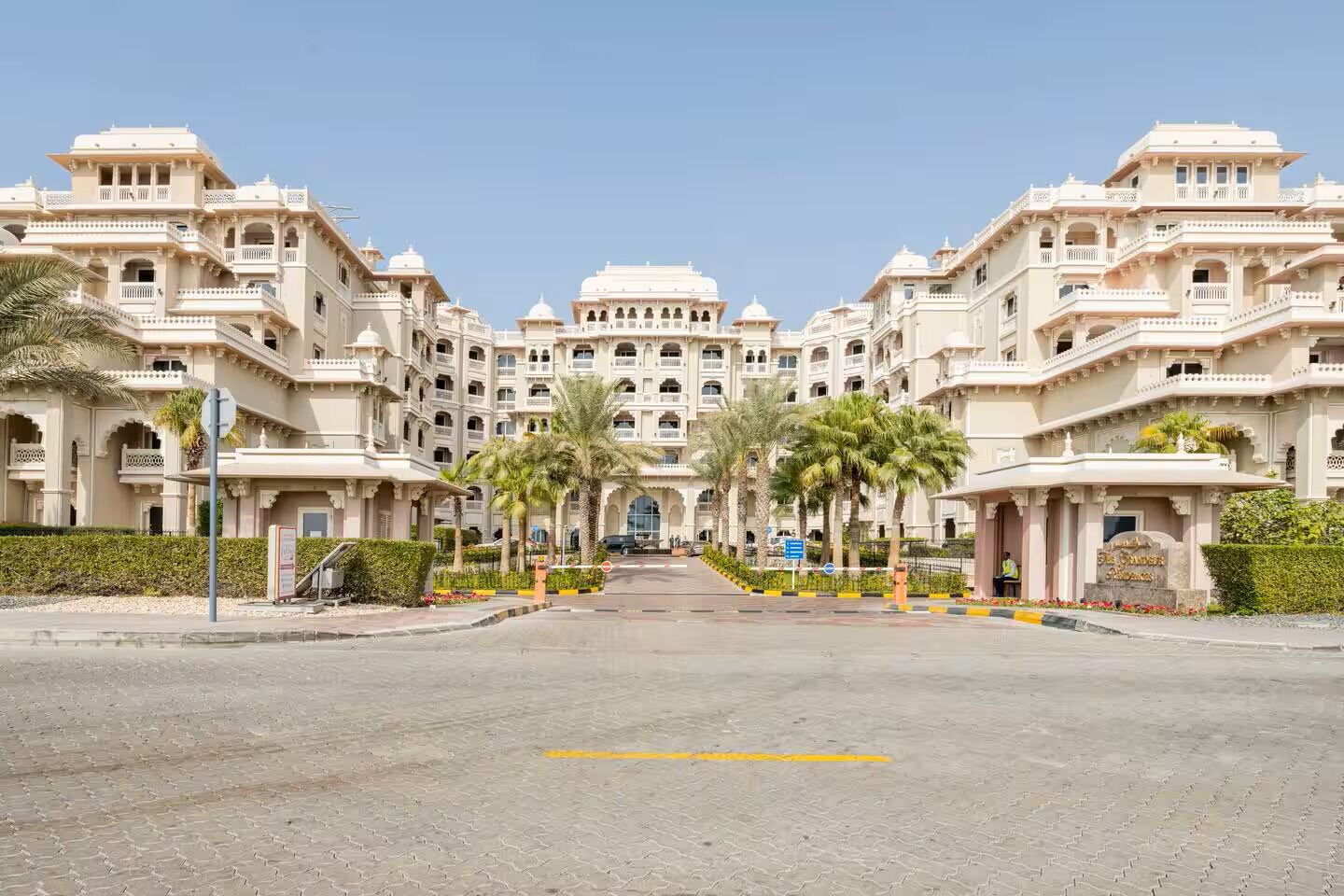 Een groot, meerhoog hotel met een symmetrische gevel, palmbomen langs de straat en een heldere lucht.