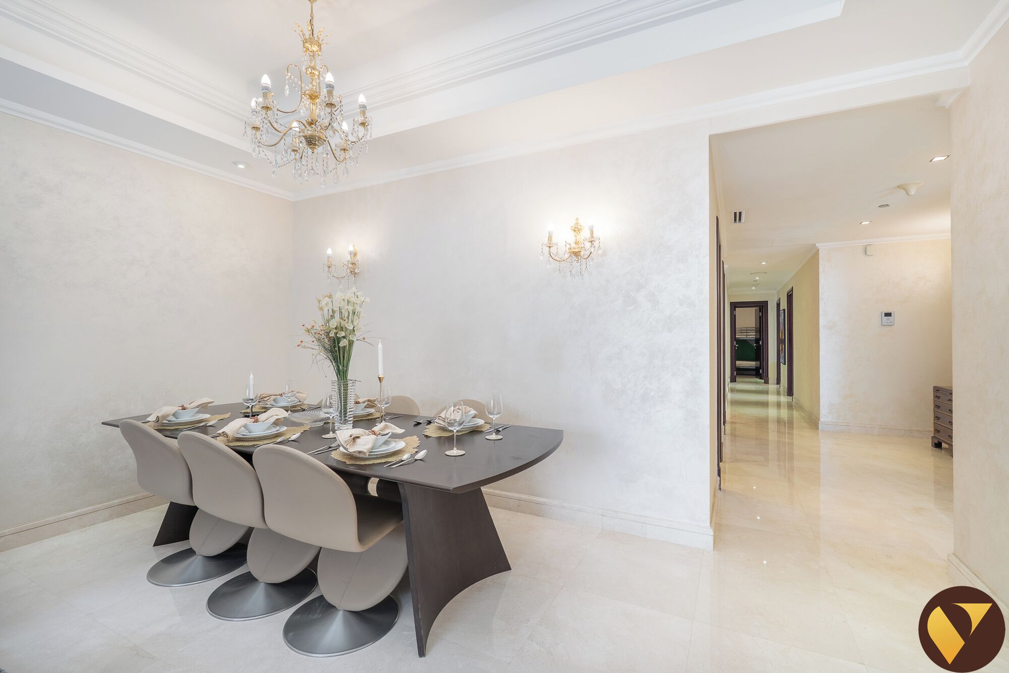 A modern dining room with a dark table, white chairs, and a chandelier.