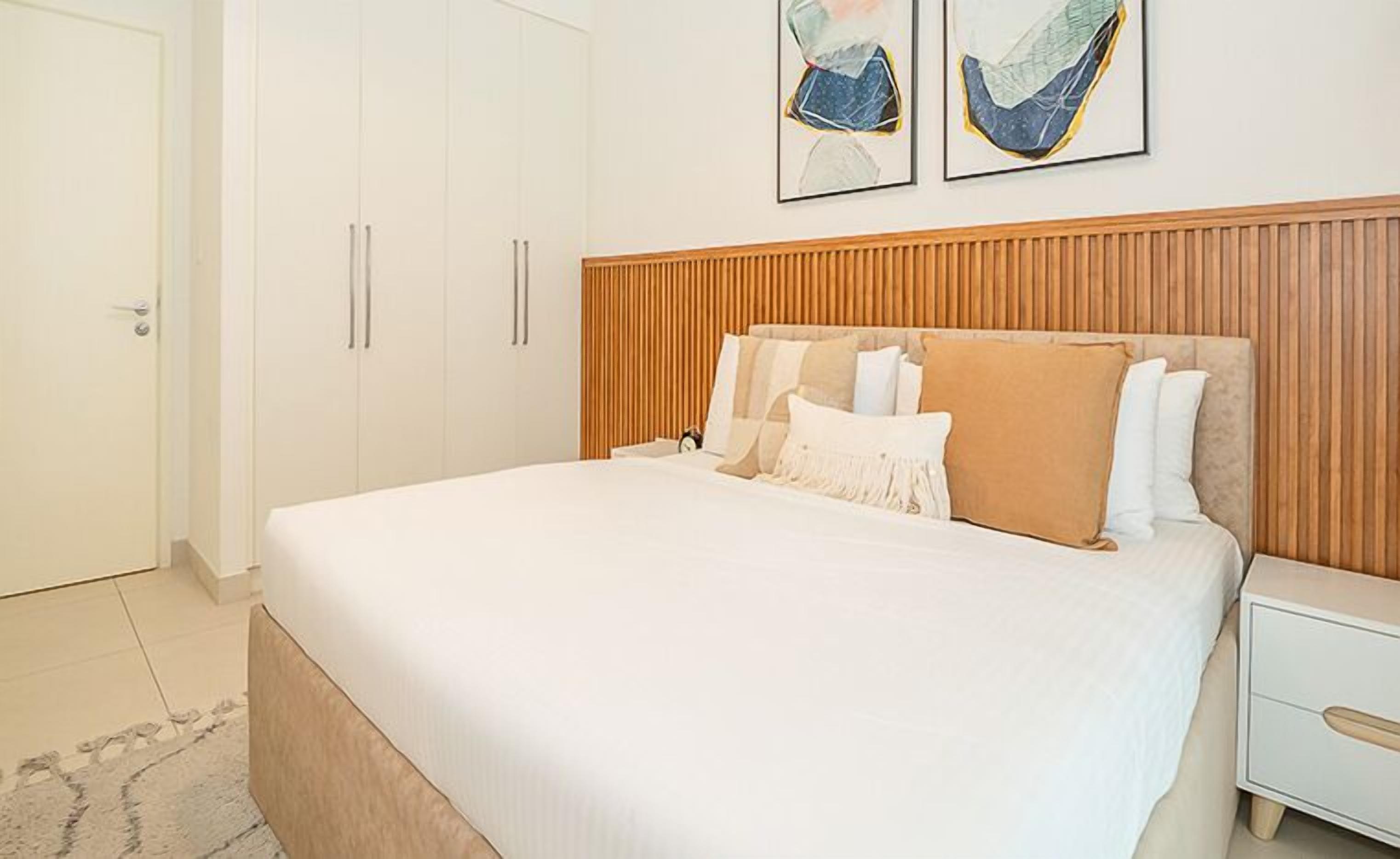 Une chambre à coucher avec un grand lit, une tête de lit en bois, des tables de chevet blanches et une porte.