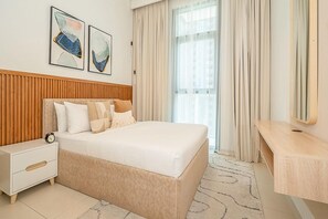 A modern hotel room with a large bed, a wooden headboard, a bedside table, a nightstand, and a large window with curtains.