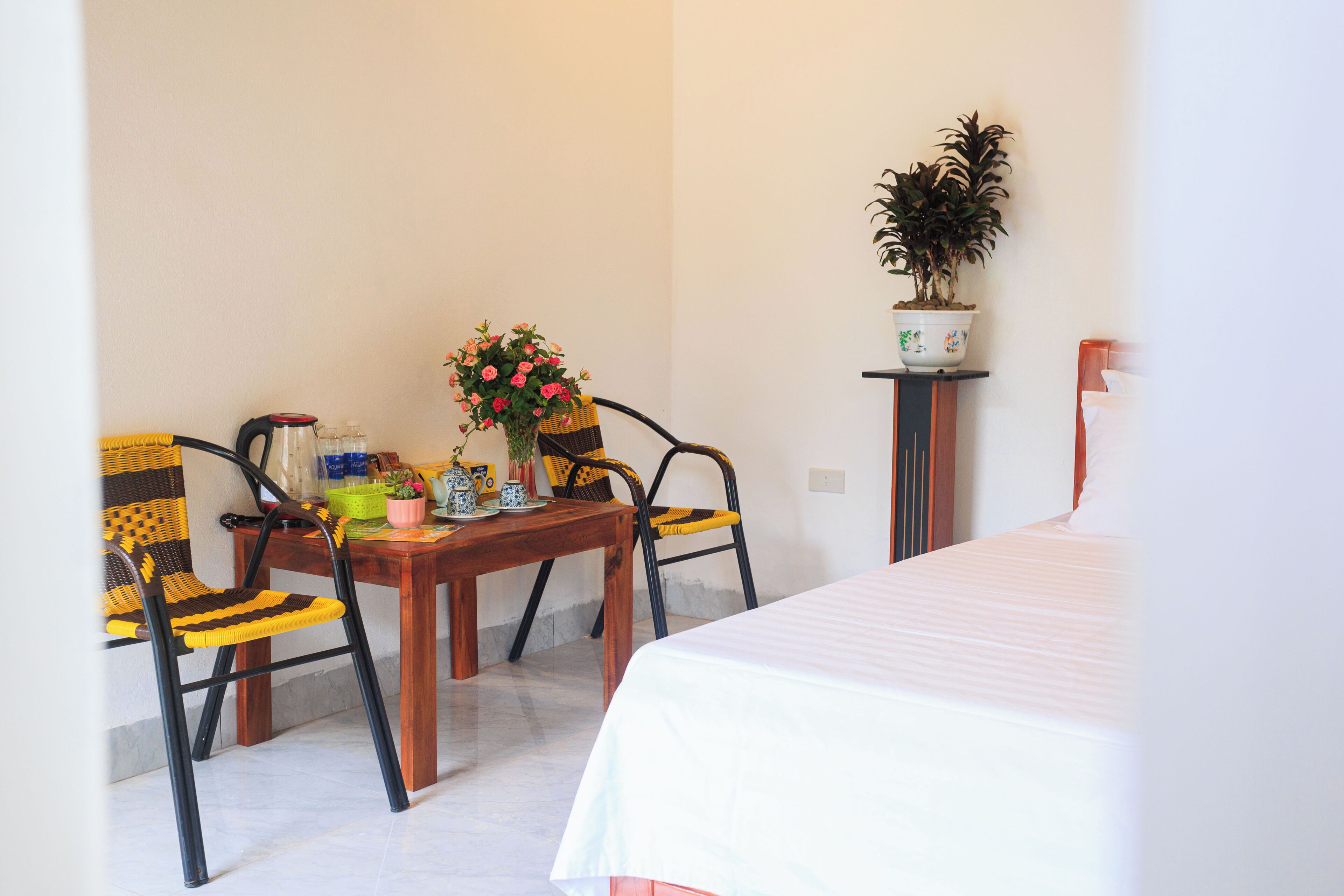 A room with a bed, a wooden table with chairs, a potted plant, and a wall-mounted shelf.