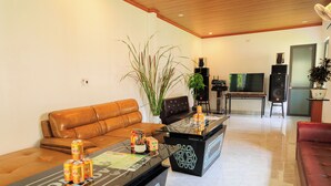 A modern living room with a brown leather sofa, a black coffee table with a geometric pattern, and a red sofa. There are speakers, a TV, and a potted plant in the room. - Heartfelt Hideaway (Nam Hoa Lu)