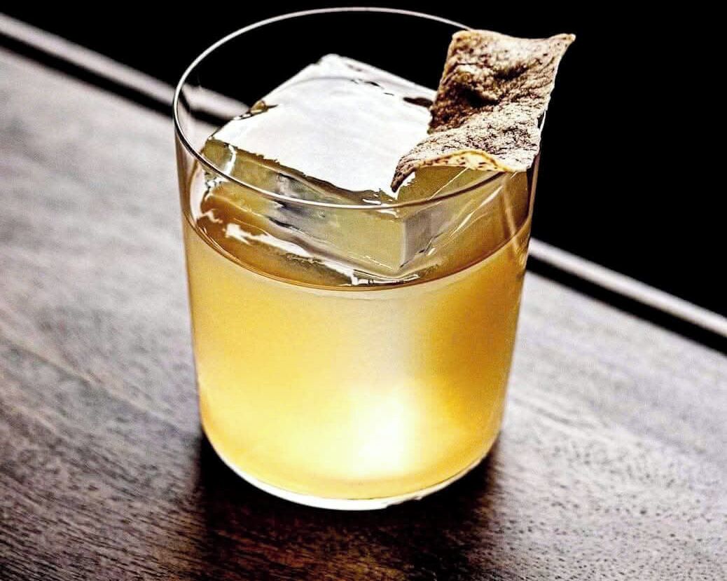 A glass with a clear liquid and a piece of brown toast on the rim.