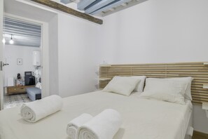 Une chambre d’hôtel comprenant un lit, deux oreillers, une tête de lit en bois, une table de chevet, une chaise, un bureau avec un ordinateur et un distributeur d’eau.