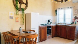 A kitchen with wooden cabinets, a white refrigerator, a stove, and a dining table with chairs. - Kampanjola in Dahlet Pawluzzu (San Lawrenz)