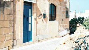 A stone building with a blue door, a small balcony, and a bicycle parked outside. - Kampanjola in Dahlet Pawluzzu (San Lawrenz)