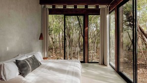A bedroom with a large window, a bed, and a view of a forest.