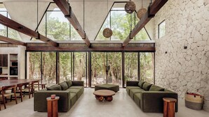 A spacious living area with a stone wall, large windows, and a high ceiling with exposed beams.