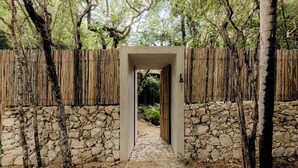 A stone pathway leading through a wooden gate into a garden area with trees and a stone wall.