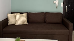 A brown sofa with patterned cushions, a white table with a woven placemat and a small plant, and three framed botanical prints on the wall. - Silv apartment3 Preveza city center (Preveza)