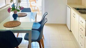 A modern kitchen with a dining area. It includes a table with chairs, a hanging light fixture, and a window with blinds. - Silv apartment3 Preveza city center (Preveza)