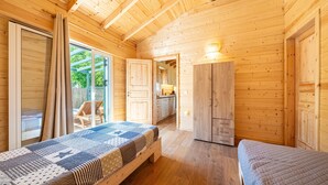A wooden cabin with two beds, a kitchen, and a sliding glass door to the outside.